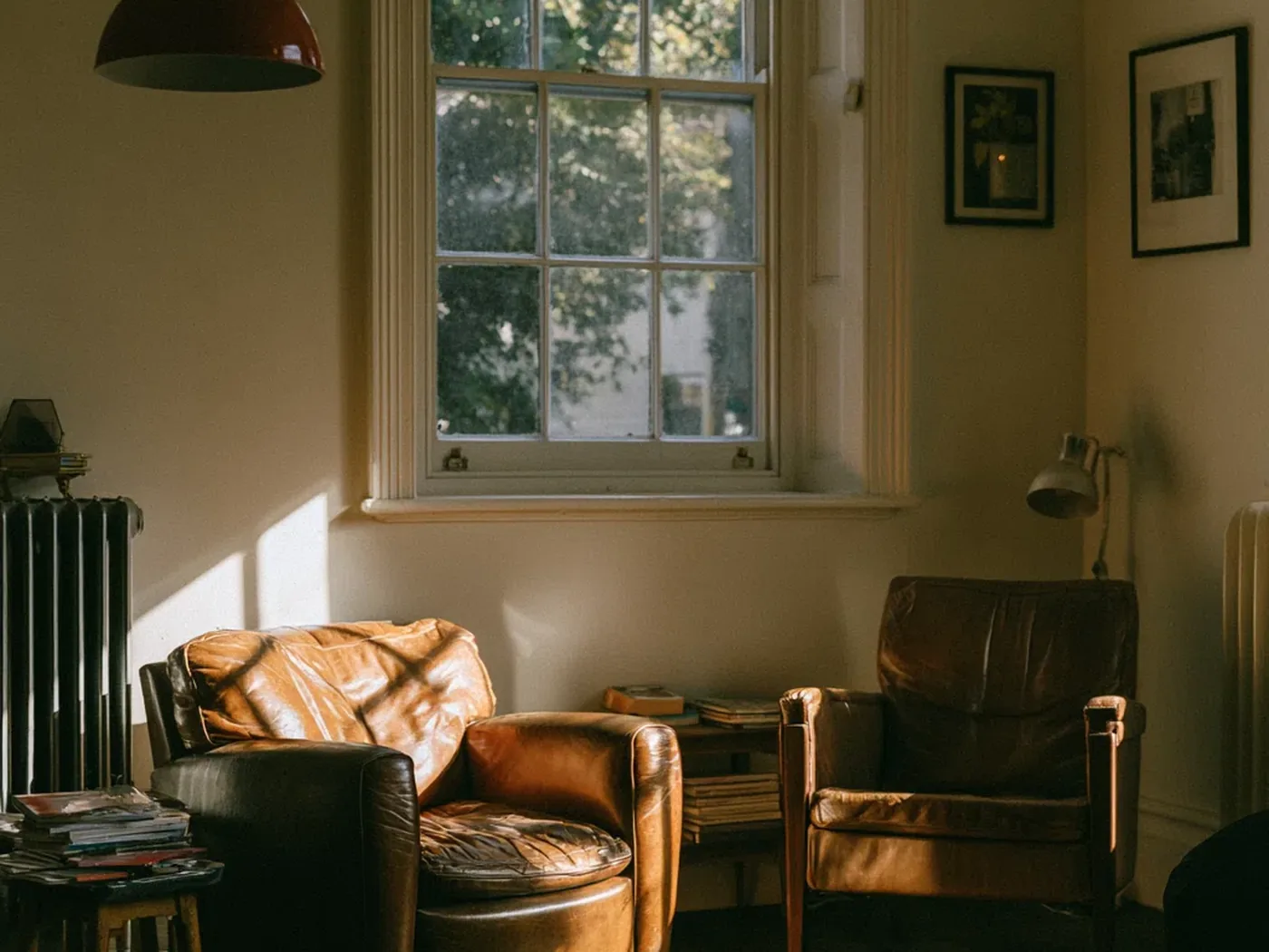 Two worn leather armchairs angled towards each other beneath a sash window, with afternoon light across the floor.